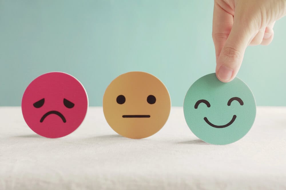 Hand choosing a smiling face from sad, neutral and happy mood cards