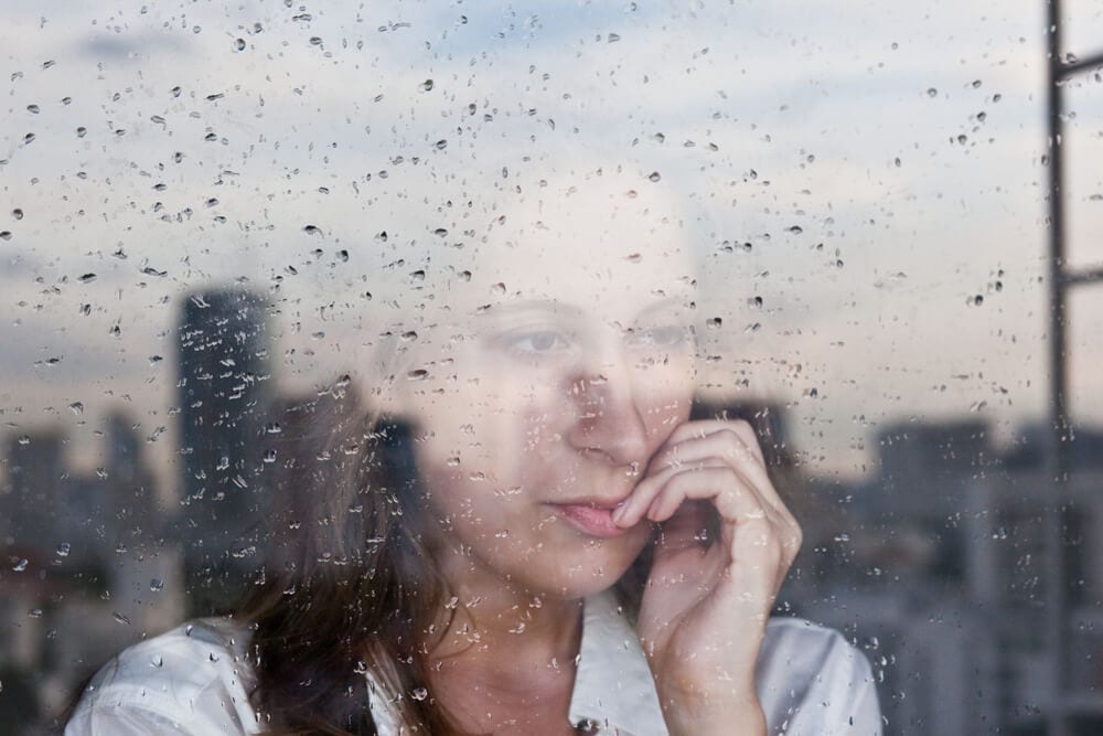 Woman looking out a rain-streaked window over the city